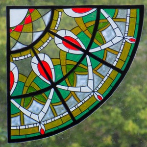 May include: A stained glass window panel with a geometric design featuring green, red, white, and gold colors. The panel is shaped like a quarter circle and has a black border.
