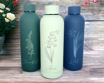 May include: Three cylindrical metal water bottles in dark green, light green, and navy blue. Each bottle features a unique engraved floral illustration and a personalised name: Charlotte on the dark green, Ann on the light green, and Kat on the navy blue.