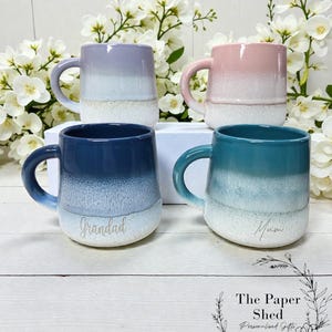 May include: Four ceramic mugs with a gradient colour scheme. The mugs are in shades of purple, pink, blue, and teal, with white bases. The mug in the bottom left has the word "Grandad" and the mug in the bottom right has the word "Mum".