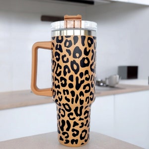 May include: A stainless steel travel mug with a brown and black leopard print design. The mug has a lid and a handle.