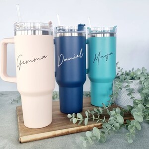 K&ouml;nnte beinhalten: Drei Edelstahl-Reisebecher mit Deckel und Strohhalmen. Die Becher sind mit den Namen "Gemma", "Daniel" und "Maya" personalisiert.