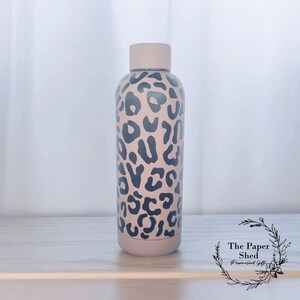 May include: A beige stainless steel water bottle with a black leopard print design. The bottle has a screw-on lid and is approximately 500 ml in size.