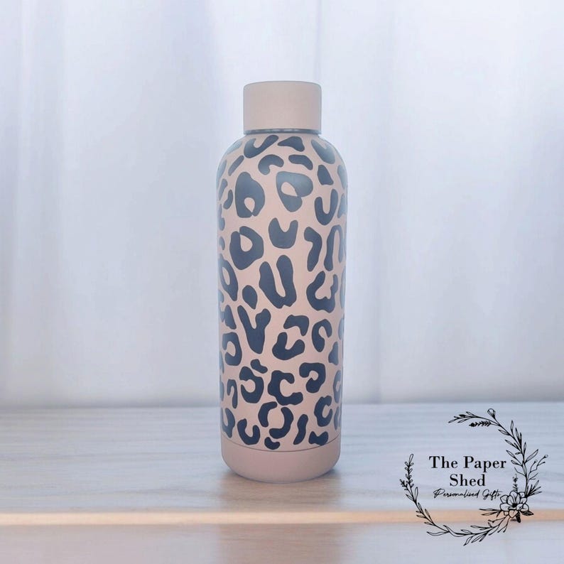 May include: A beige stainless steel water bottle with a black leopard print design. The bottle has a screw-on lid and is approximately 500 ml in size.