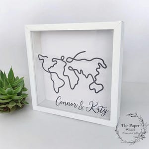 May include: White shadow box with a black line drawing of the world map and the text "Connor & Katy" at the bottom.