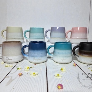 May include: Eight ceramic mugs arranged in two rows, featuring a two-tone ombre glaze with a speckled white base. The mugs come in various colours including cream, light blue, lavender, pink, brown, dark blue, teal, and black, with names printed.
