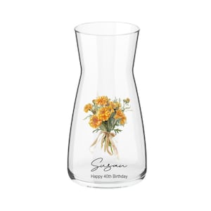 May include: A clear glass carafe featuring a bouquet of orange flowers tied with a beige ribbon. The carafe is inscribed with the name "Susan" and the message "Happy 40th Birthday".