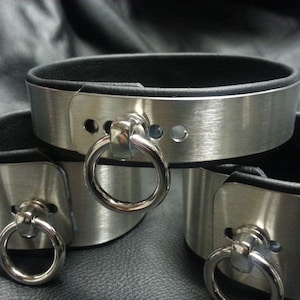 Puede incluir: Tres brazaletes de metal plateado con forro de cuero negro y un anillo plateado en cada brazalete.