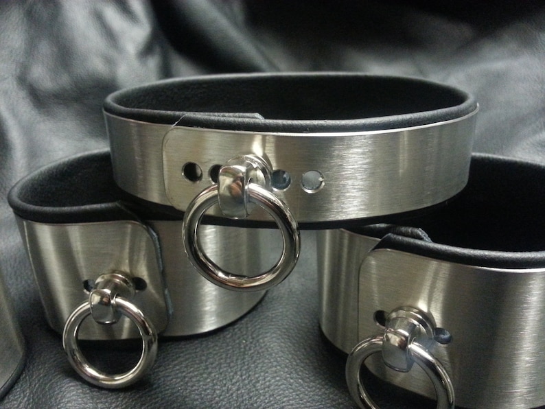 Puede incluir: Tres brazaletes de metal plateado con forro de cuero negro y un anillo plateado en cada brazalete.