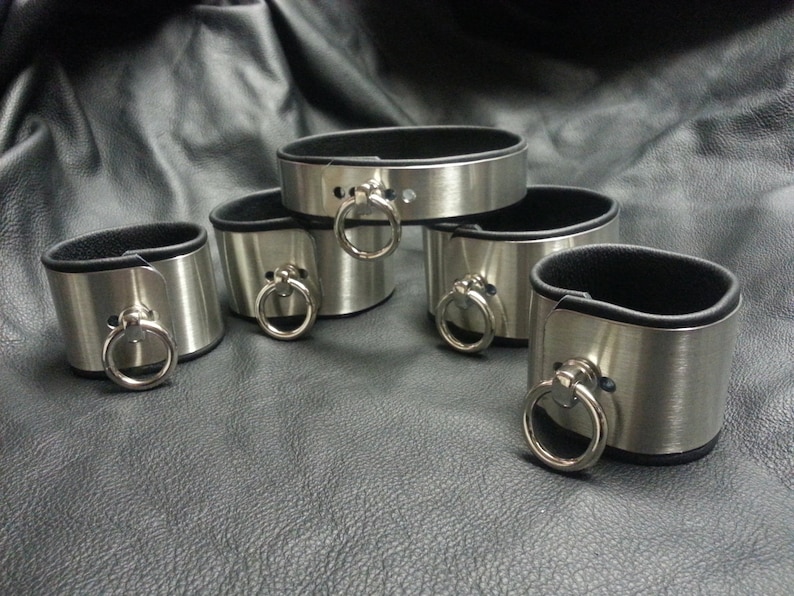 Puede incluir: Cinco brazaletes de metal plateado con forro de cuero negro y un anillo plateado en cada brazalete.