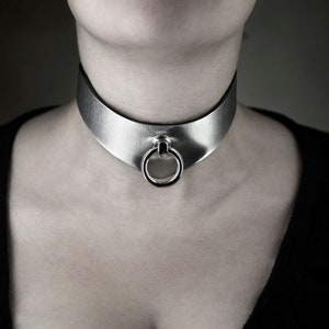 May include: A silver choker necklace with a large, round ring in the center.
