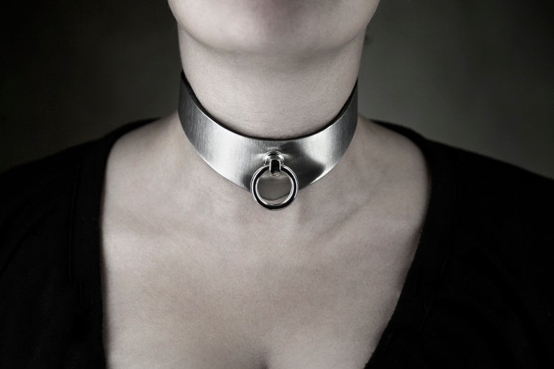 May include: A silver choker necklace with a large, round ring in the center.