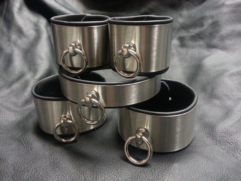 Puede incluir: Cuatro brazaletes de metal plateado con forro de cuero negro y un anillo plateado en cada brazalete.