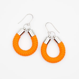 Op de afbeelding: Een paar oranje touw oorbellen met zilveren haken en metalen accenten. De oorbellen zijn hoefijzervormig.