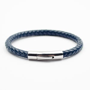 May include: A navy blue braided leather bracelet with a silver-colored clasp. The bracelet is circular and appears to be approximately 8 inches in circumference. The clasp is a simple, rectangular design.