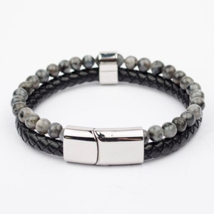 Puede incluir: Un brazalete de cuero negro con cierre magnético plateado y cuentas de piedras grises.