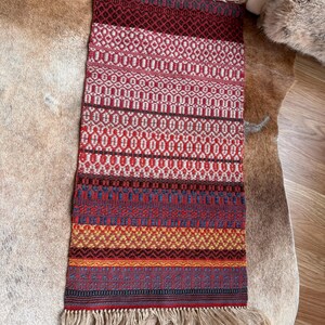 May include: A colorful woven rug with a geometric pattern in shades of red, orange, yellow, blue, and white. The rug has a fringe border.