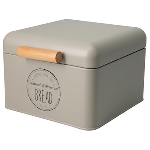Könnte beinhalten: Eine graue Brotbox aus Metall mit einem Holzgriff. Die Box hat abgerundete Ecken und einen Deckel. Auf der Vorderseite der Box befindet sich ein kreisförmiges Design mit den Worten "Homemade with Love, Natural & Premium, BREAD, Since 1951."