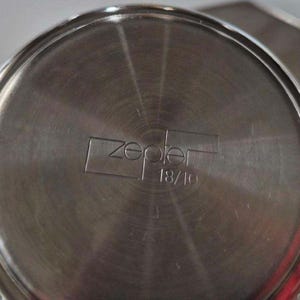 Puede incluir: Primer plano de la base de una olla de acero inoxidable con la marca "zepter" y "18/10" grabadas en el metal. La olla tiene un dise&ntilde;o circular con l&iacute;neas conc&eacute;ntricas que irradian desde el centro.