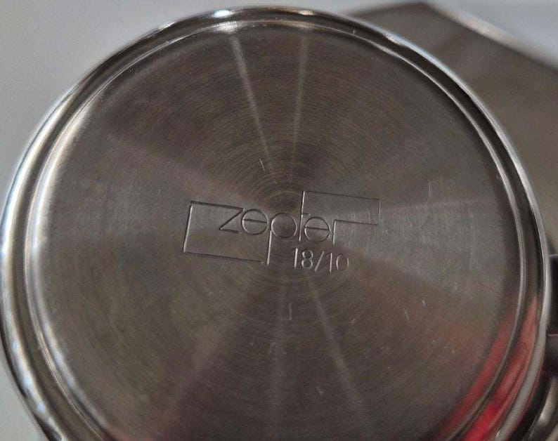 Puede incluir: Primer plano de la base de una olla de acero inoxidable con la marca "zepter" y "18/10" grabadas en el metal. La olla tiene un dise&ntilde;o circular con l&iacute;neas conc&eacute;ntricas que irradian desde el centro.