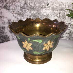 Könnte beinhalten: Eine Schale aus Messing mit einem gewellten Rand und einem dunkelblauen Boden. Die Schale ist mit handbemalten gelben Blumen und grünen Blättern verziert.