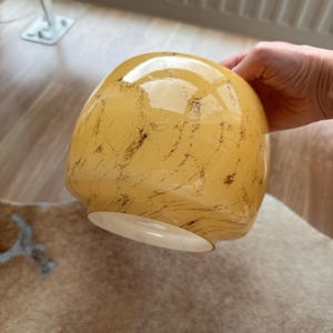 Op de afbeelding: Een afgeronde glazen lampenkap met een glanzende lichtgele afwerking en een donkerbruin gemarmerd of geaderd patroon over het hele oppervlak. De binnenkant van de glazen kap is wit en de opening aan de onderkant heeft een gladde, ronde rand.