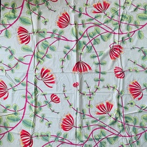 Puede incluir: Tela blanca con un estampado floral repetitivo. El diseño presenta flores rojas en forma de abanico con detalles amarillos, hojas verdes y tallos rosas. El patrón se extiende por la tela.