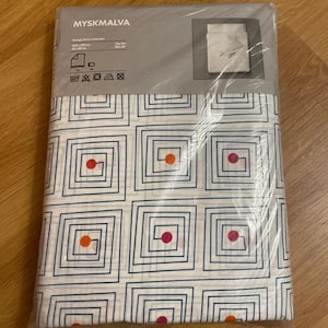 Könnte beinhalten: Ein verpacktes Bettwäsche-Set mit geometrischem Muster. Die Bettwäsche hat einen weißen Hintergrund mit blauen quadratischen Mustern, die jeweils einen roten oder orangen Punkt enthalten. Die Verpackung trägt die Aufschrift "MYSKMAVA". Die Maße sind 200x200 cm und 90x90 cm.