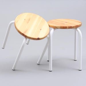 Può includere: Due sgabelli in legno con sedili rotondi colorati chiari e gambe in metallo bianco. Uno sgabello è inclinato, mostrando la venatura naturale del legno del sedile. L'altro sgabello è in posizione verticale. Gli sgabelli sono semplici e moderni. I sedili hanno un diametro di circa 30 cm.