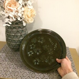 May include: A dark green ceramic plate with a decorative design of white and blue floral patterns. The plate is round and has a slightly raised rim.