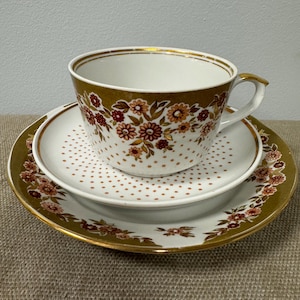 May include: A white ceramic teacup and saucer set featuring a gold band and a floral pattern with red and orange flowers. The teacup has a polka dot design on the lower half, while the saucer features a wide gold border with a floral motif.