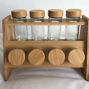 May include: A bamboo spice rack with four clear glass jars and wooden lids. The rack has a two-tiered design, with four additional wooden lids at the bottom. The rack is made of light brown bamboo.