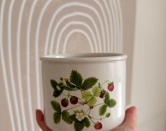 May include: White ceramic planter with a strawberry design. The planter features green leaves, white flowers, and red strawberries.