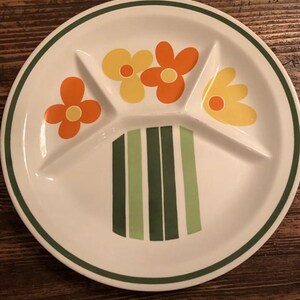 Könnte beinhalten: Weißer Teller mit grüner Umrandung und Blumendesign. Der Teller hat drei Fächer und ist mit orangefarbenen und gelben Blumen verziert. Der Boden des Tellers hat grüne und dunkelgrüne vertikale Streifen.