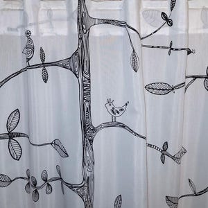 Op de afbeelding: Witte gordijn met een zwart boom- en vogelontwerp. De boomstam en takken zijn zwart omlijnd, met bladeren en vogels verspreid. De vogels zijn eenvoudige, cartoonachtige figuren.