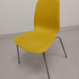 May include: A bright yellow chair with a curved back and seat. The chair has four silver metal legs. The chair is made of a smooth, solid material and is set against a white brick wall.