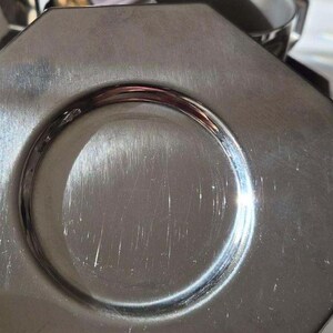 Puede incluir: Primer plano de un plato octogonal plateado con una hendidura circular en el centro. El plato tiene una superficie brillante y reflectante con ara&ntilde;azos visibles.