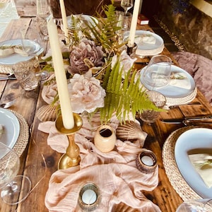 Peut inclure: Une table en bois rustique avec une composition florale de fougères et de fleurs roses. La table est décorée de chandeliers dorés, de bougies chauffe-plat et d'un chemin de table rose transparent. Les couverts comprennent des assiettes blanches, des dessous-de-plat en osier et des serviettes.