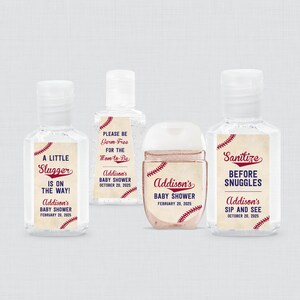 May include: Four small, clear hand sanitizer bottles with baseball-themed labels. The labels feature phrases like "A Little Slugger is on the Way!" and "Sanitize Before Snuggles." The text includes baby shower details.