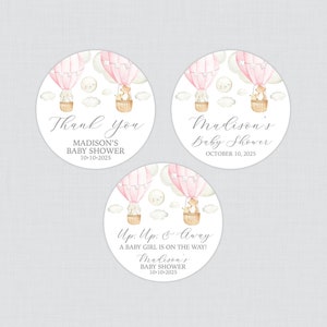 May include: Three round pink and white baby shower favor stickers with a hot air balloon theme. The stickers feature a pink hot air balloon with a fox and a bear in a basket. The text on the stickers reads "Thank you Madison's Baby Shower 10-10-2025", "Madison's Baby Shower October 10, 2025", and "Up, Up & Away A baby girl is on the way! Madison's Baby Shower 10-10-2025".