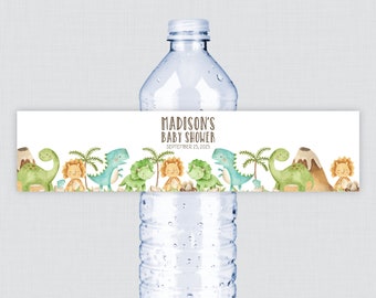 May include: Water bottle label with a dinosaur theme. The label is white with brown text that reads "Madison's Baby Shower" and "September 25, 2015". The label features a row of cartoon dinosaurs, palm trees, and a volcano.