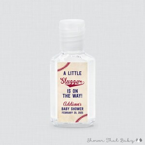May include: Clear hand sanitizer bottle with a white cap. The label reads "A LITTLE Slugger IS ON THE WAY!" with the name "Addison's" and the date "FEBRUARY 20, 2025" in red and navy blue. Baseball theme.