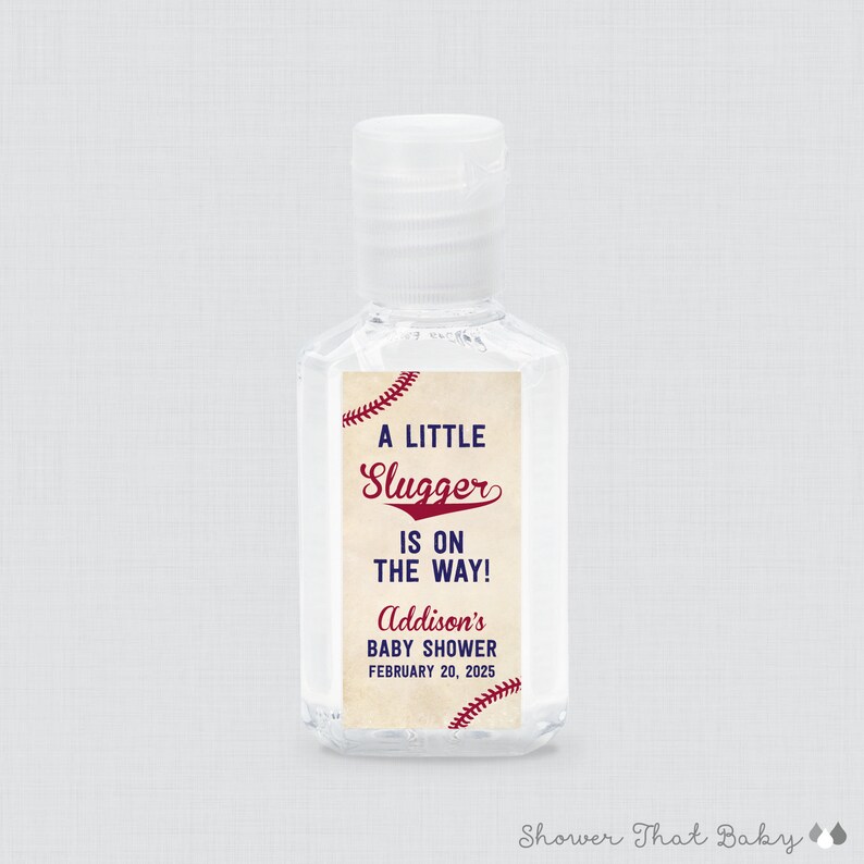 May include: Clear hand sanitizer bottle with a white cap. The label reads "A LITTLE Slugger IS ON THE WAY!" with the name "Addison's" and the date "FEBRUARY 20, 2025" in red and navy blue. Baseball theme.
