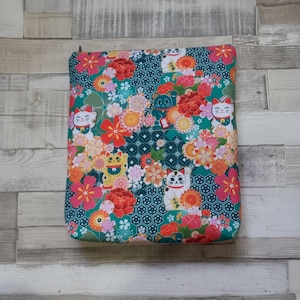 May include: A rectangular fabric pouch featuring a teal background with a repeating geometric pattern. The surface is decorated with colourful illustrations of beckoning cats, red and orange peonies, and various small pink and yellow flowers.