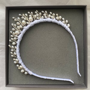 May include: A white pearl headband with a satin ribbon. The headband is decorated with small white pearls and is in a grey box.