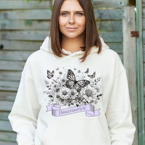 May include: White hooded sweatshirt with a black and white butterfly and floral design. The text "Be Remembered by the Flowers You Grow" is printed on a purple banner.