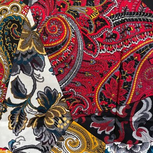 May include: A patchwork fabric with a paisley design in red, black, gold, and white. The fabric has a floral pattern in the lower left corner.