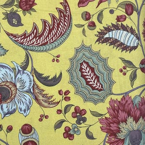May include: A yellow fabric with a floral pattern. The flowers are red, blue, and green. The fabric has a paisley design.