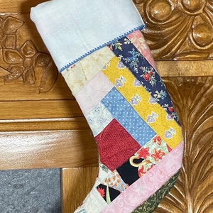May include: A patchwork Christmas stocking with a white cuff and a variety of colorful fabrics, including pink, yellow, blue, red, and green.