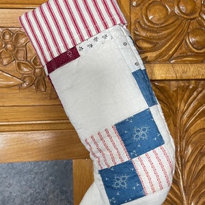 May include: A white, red, and blue patchwork Christmas stocking with a red and white striped cuff.