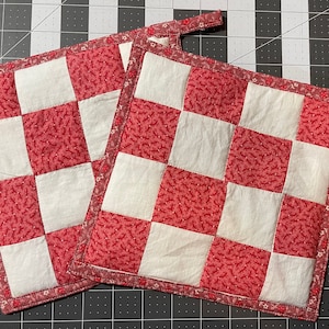May include: Two red and white checkered pot holders with a floral pattern. The pot holders have a loop for hanging.